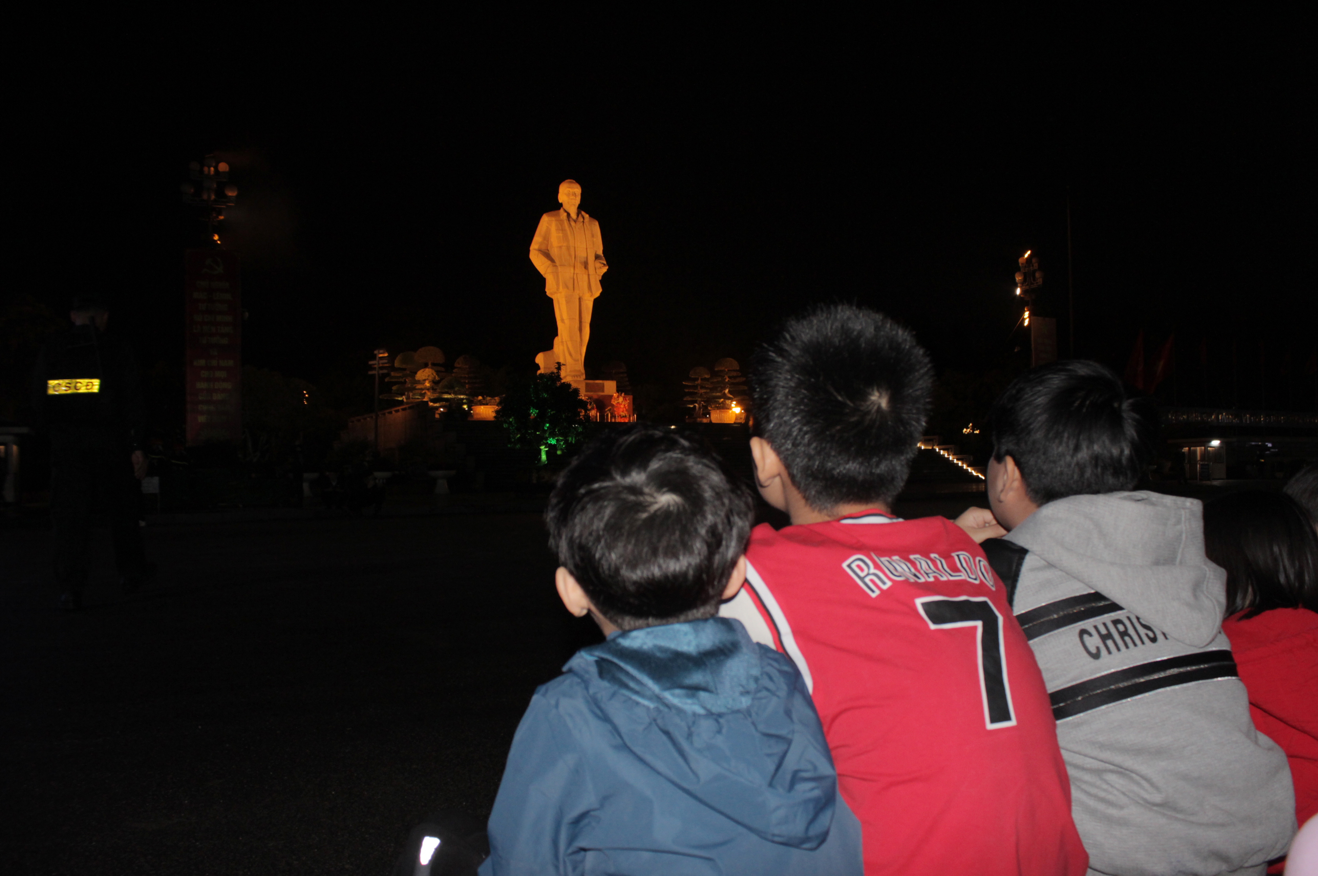Children sit and watch Uncle Ho's statue.